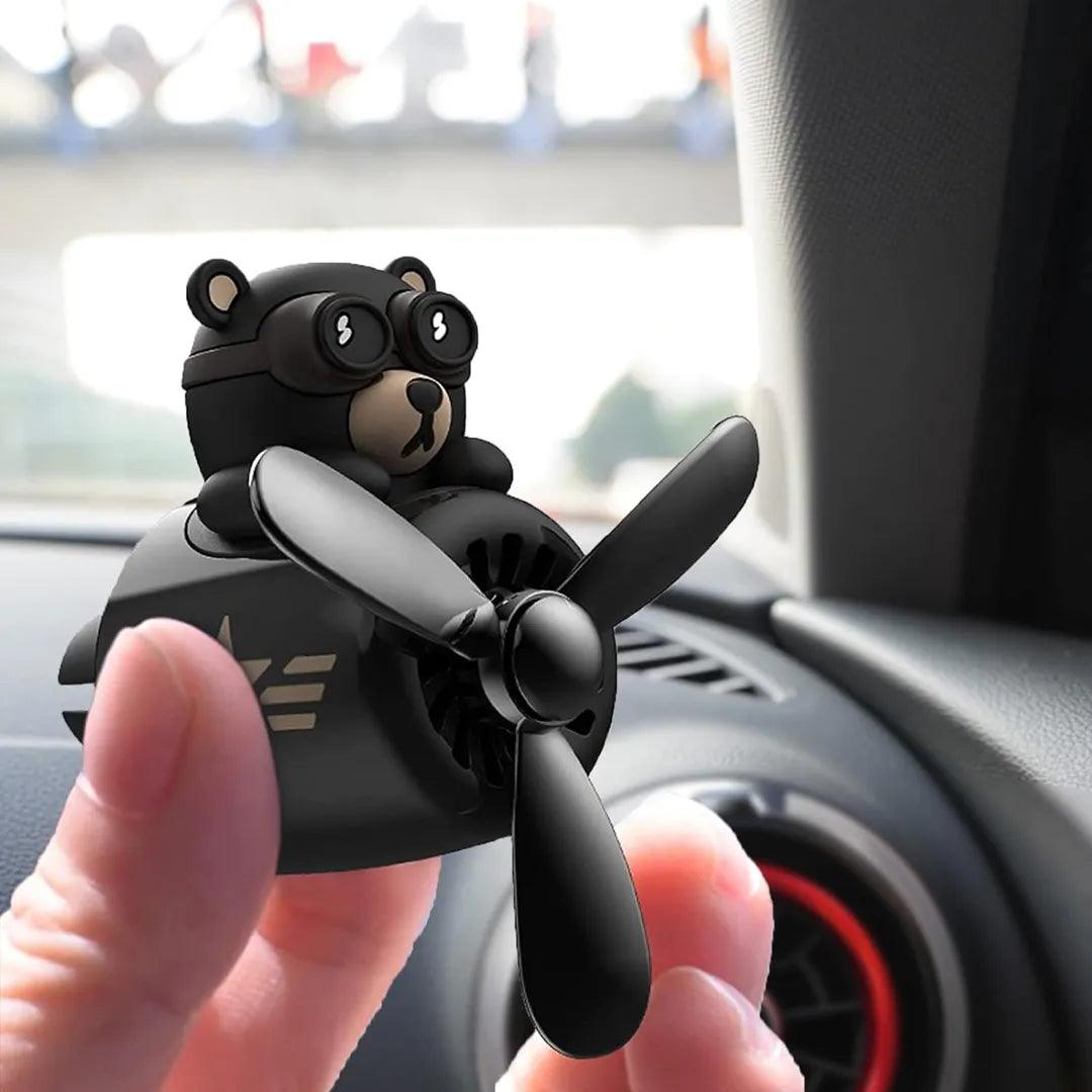 Bear pilot-themed car air freshener being held near a car air vent, showcasing its compact and portable design.