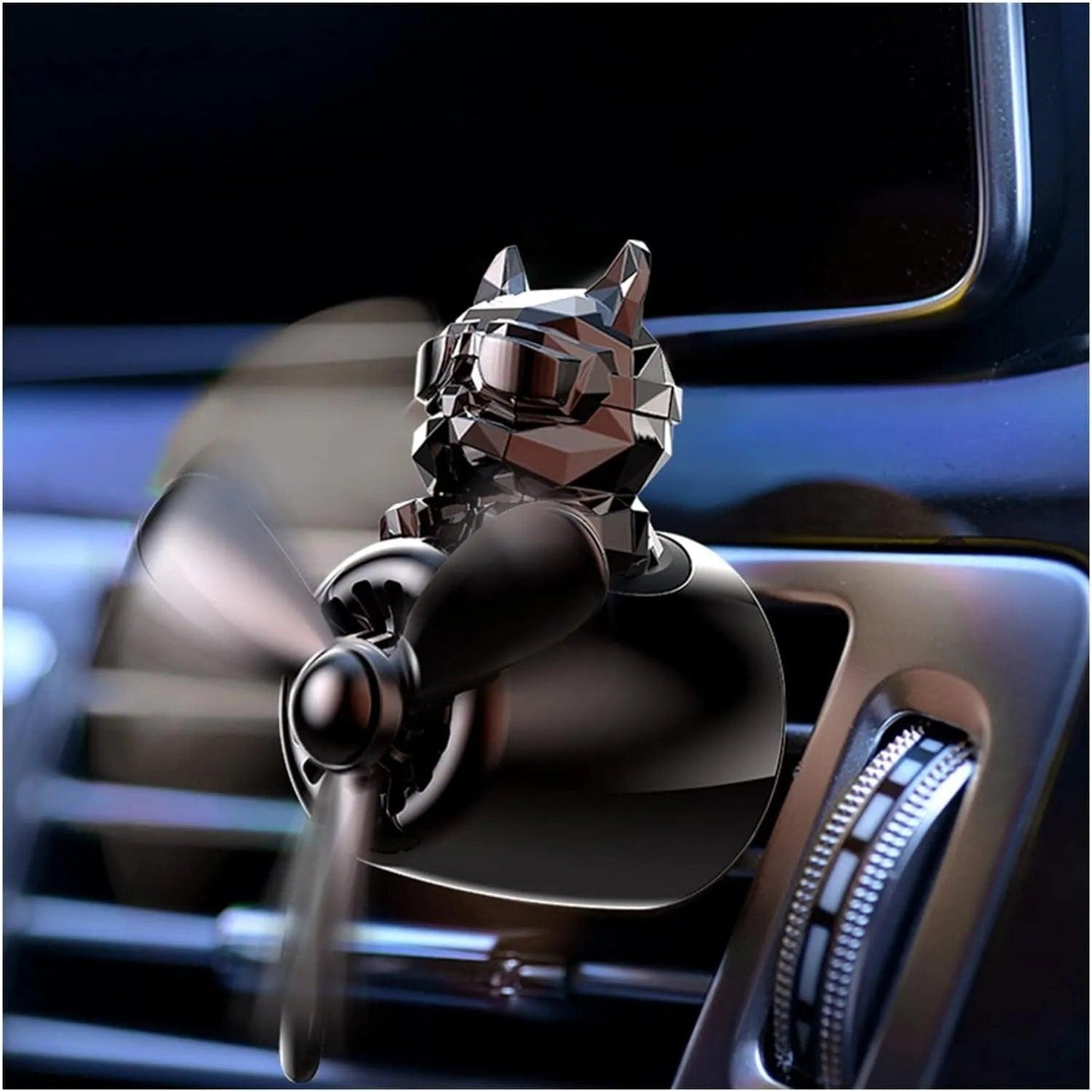 The image shows a bulldog pilot car air freshener with a propeller design attached to the car's air vent. The bulldog figure has a sleek, faceted surface and is wearing aviator goggles. The propeller is spinning, indicating that the air freshener is actively dispersing fragrance into the car. The background shows part of the car's dashboard and air vent controls.