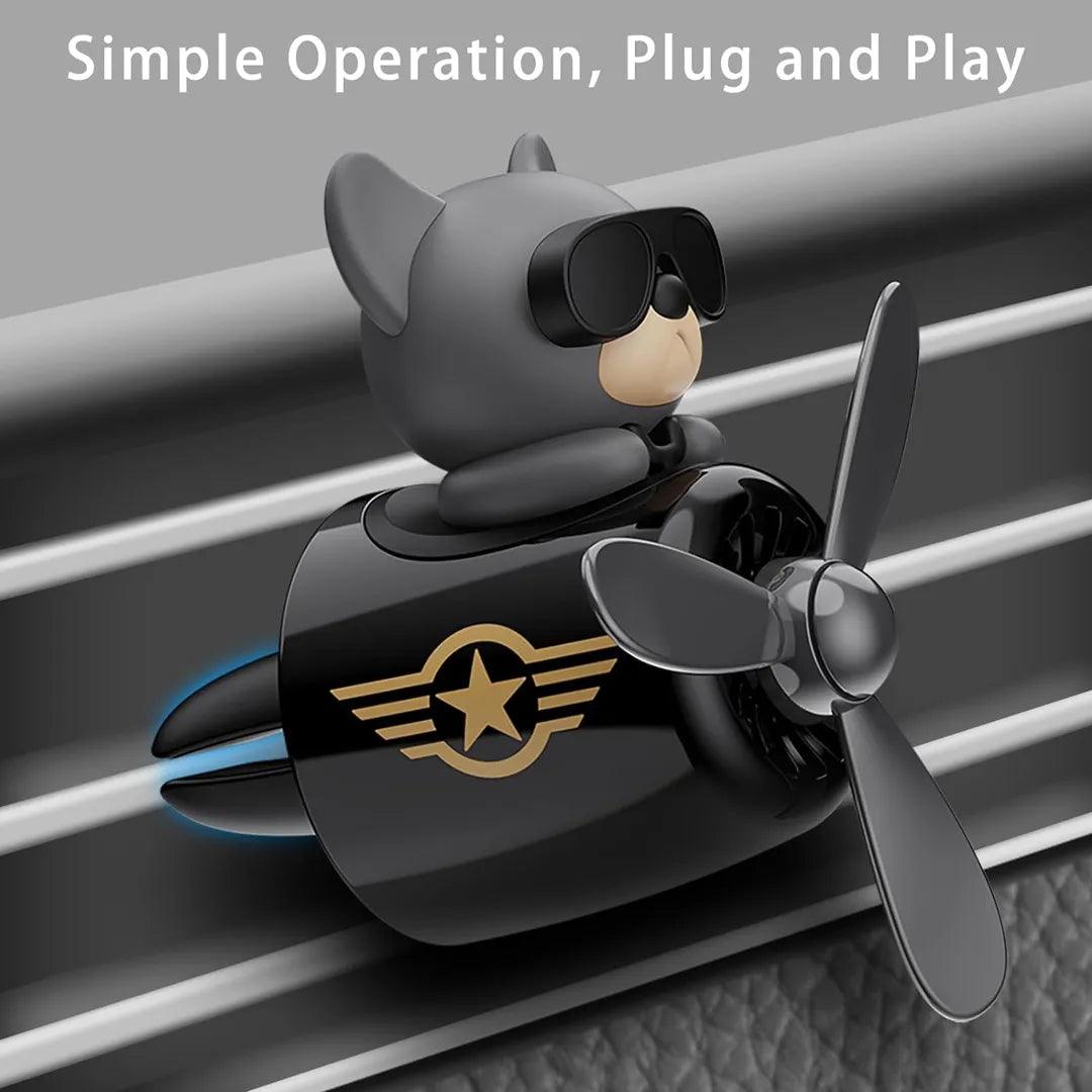 The image shows a car air freshener designed as a dog pilot with sunglasses. The air freshener features a propeller and a star emblem, and is clipped onto a car vent. The text "Simple Operation, Plug and Play" highlights its ease of use.