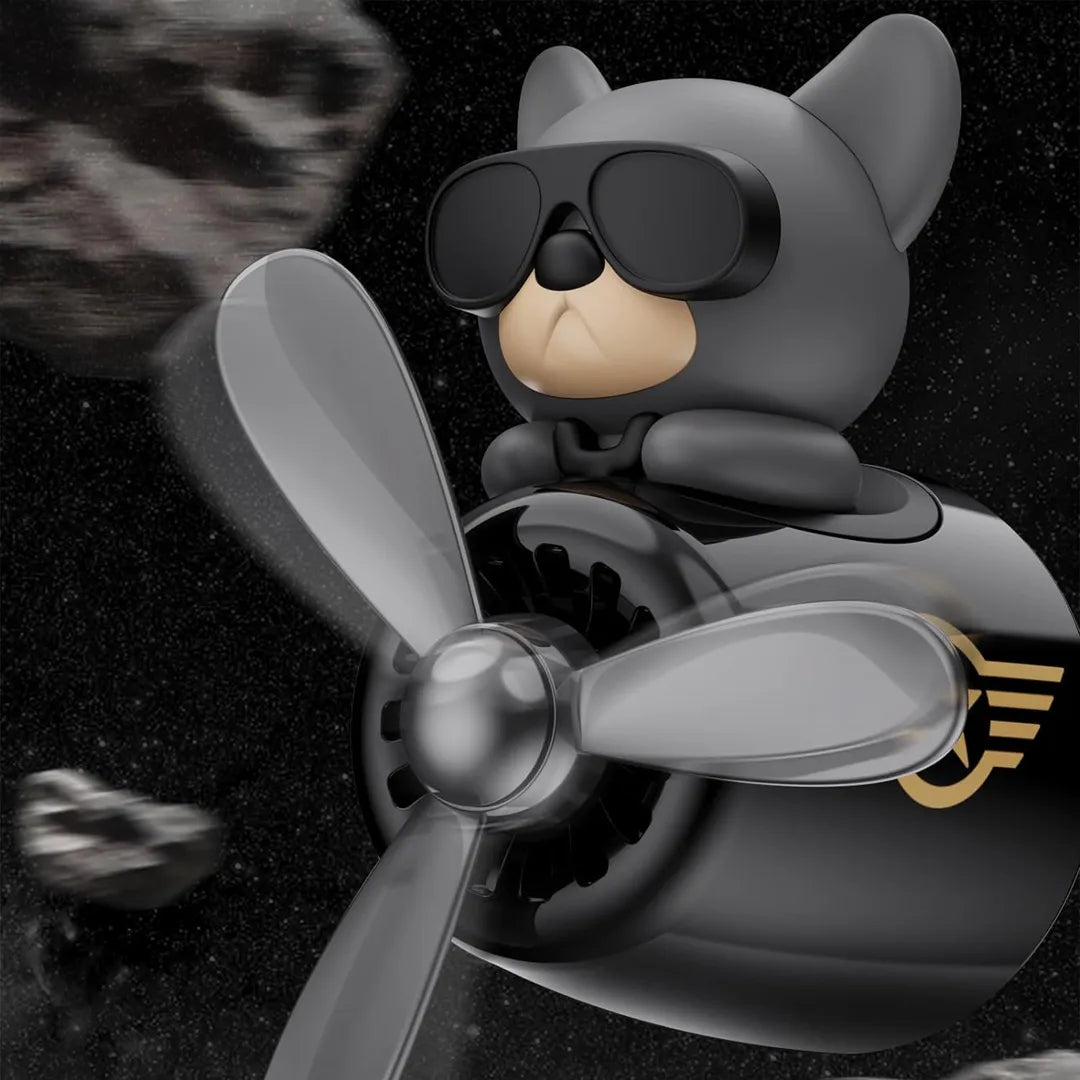 The image shows a car air freshener designed as a dog pilot with sunglasses, featuring a propeller and a star emblem. The background depicts the dog pilot in space, with a blurred asteroid in the distance, emphasizing an adventurous and playful theme.