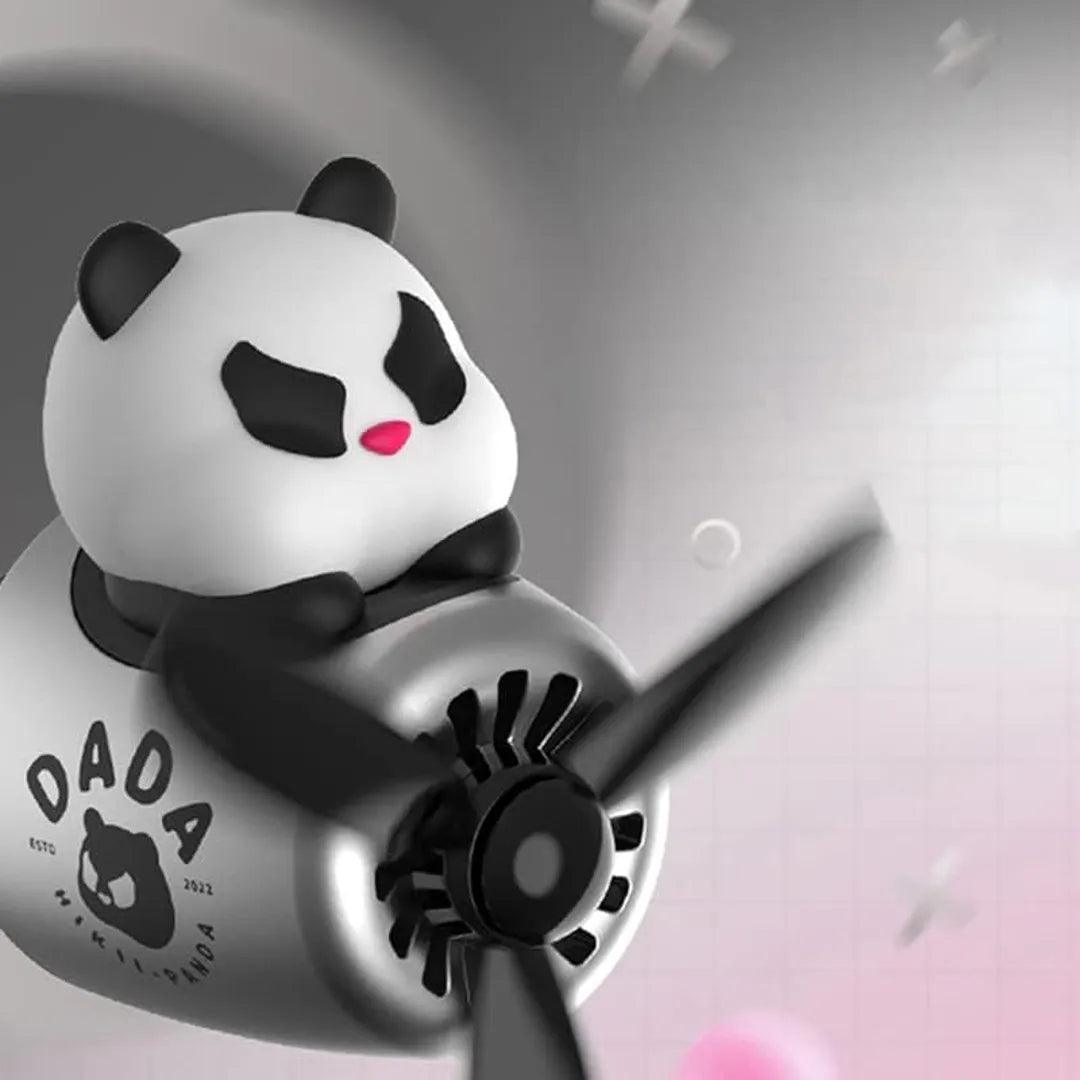 A panda-themed car air freshener with a black propeller, mounted on a silver and black airplane-shaped body. The panda figure sits on top with a pink nose and black eye patches. The text on the body reads 'DADA' with a panda logo and 'ESTD 2022'. The background is grey with some abstract shapes.