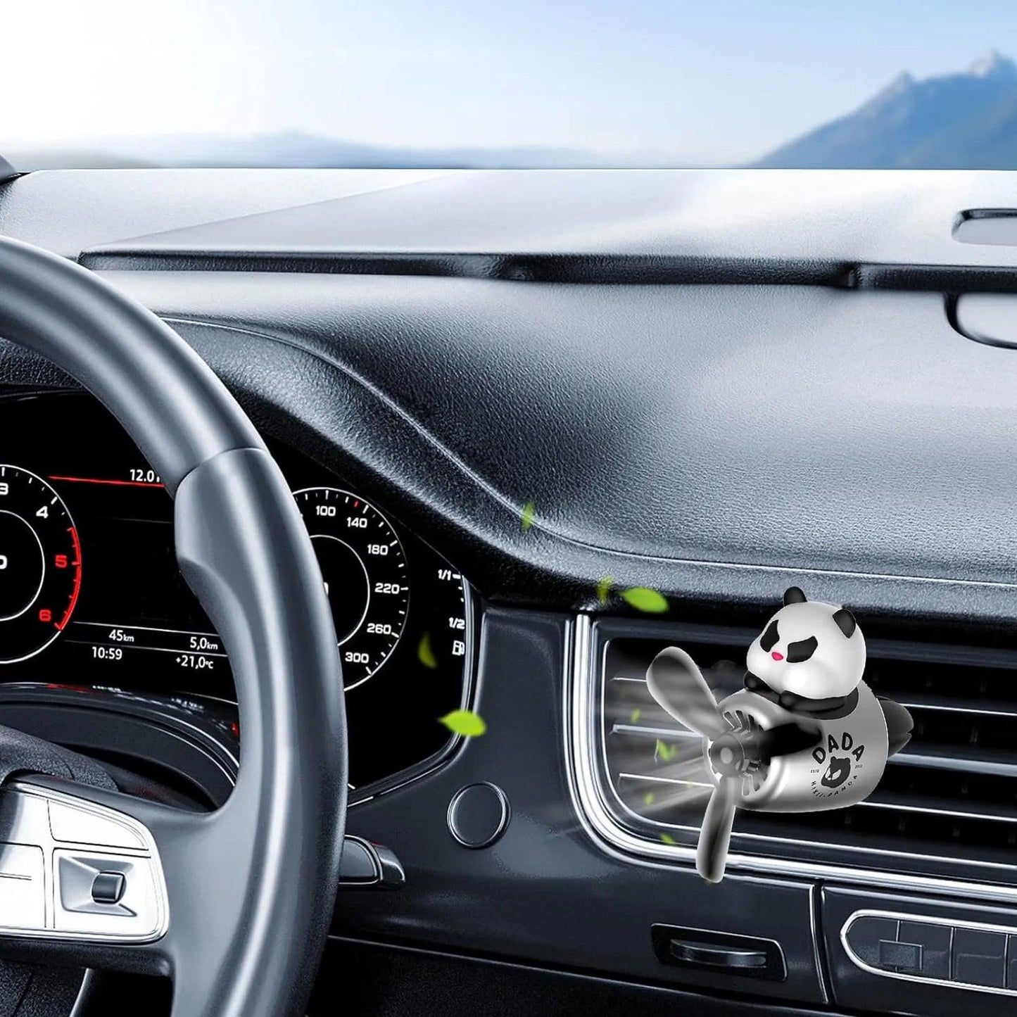 A panda-themed car air freshener attached to the air vent of a car's dashboard. The interior of the car includes a steering wheel and a dashboard with speed and other gauges. The background shows a scenic view outside the car