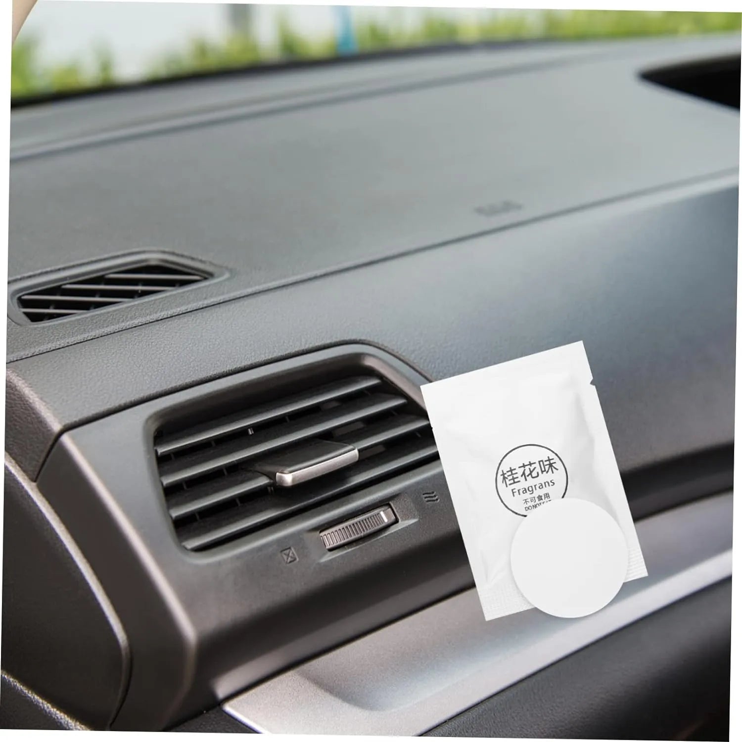 Car air vent with a Fragrans air freshener packet and a round air freshener tablet.